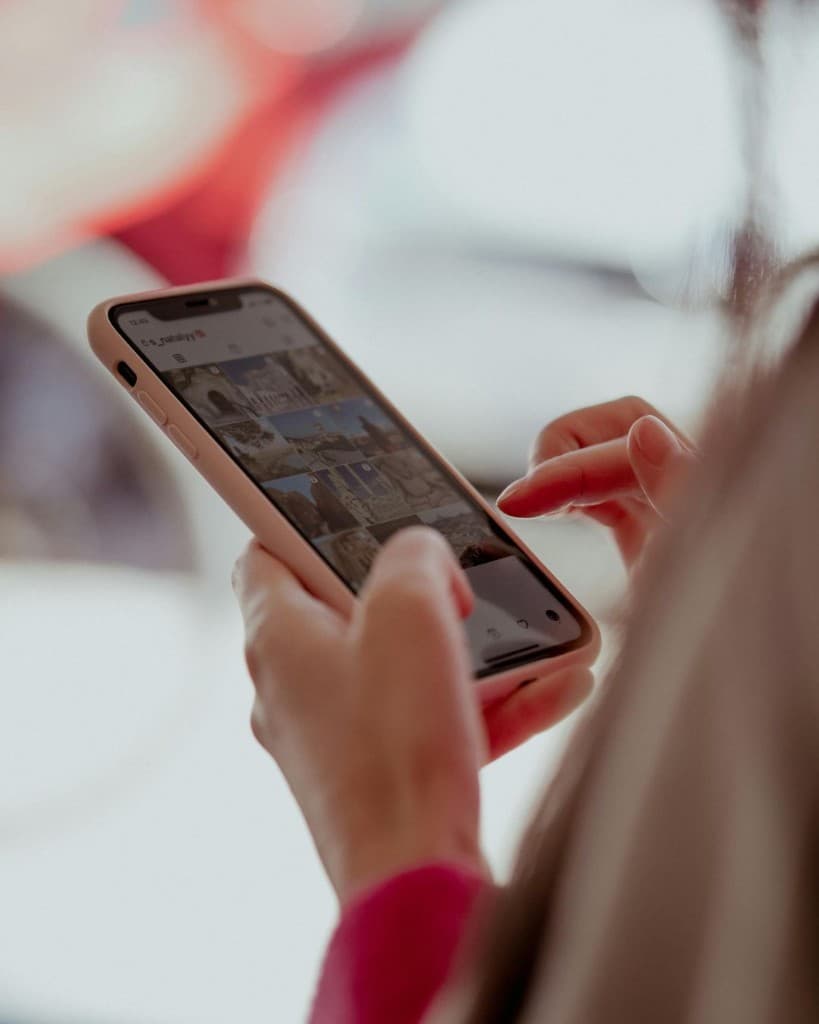 Hands holding a smartphone showing a social media profile grid in the feed